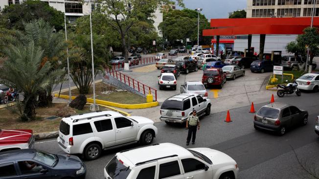 Un oficial de policía controla el tráfico mientras las personas esperan en fila para llenar los tanques de sus autos en una gasolinera de la petrolera estatal PDVSA en Caracas.
