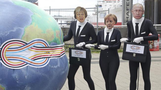 Activistas disfrazados de Theresa May, Angela Merkel y Vlaímir Putin estrujan un globo terráqueo durante una acción de protesta organizada por el grupo Attac contra la globalización en Hamburgo.