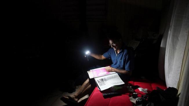Por la falta de electricidad, Hugo Regalado lee el periódico con la ayuda de una linterna en medio de una oscura noche en la isla.