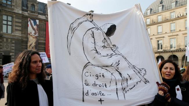 Manifestantes sostienen una pancarta que dice "aquí yace el derecho al asilo" en París.