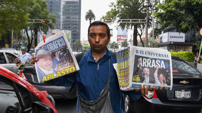 Un vendedor de periódicos en México con dos ejemplares en los que su información principal es el triunfo de Andrés Manuel López Obrador.