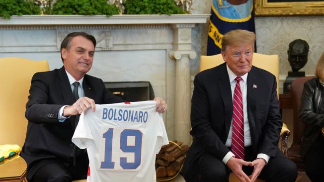 El presidente de Estados Unidos, Donald Trump (d), entrega una camiseta oficial de la selección de fútbol estadounidense a su homólogo brasileño, Jair Bolsonaro (i).