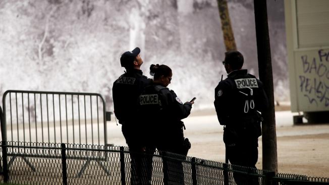 Tres policías montan guardia frente a la Torre Eiffel mientras un hombre escala por el monumento, este lunes en París (Francia).