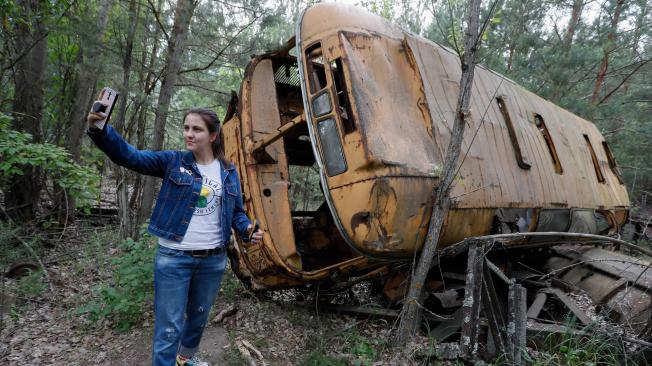 Una mujer se fotografía junto a un autobús abandonado durante una visita guiada a Chernóbil (Ucrania), en donde los efectos de la radiación han disminuido considerablemente.