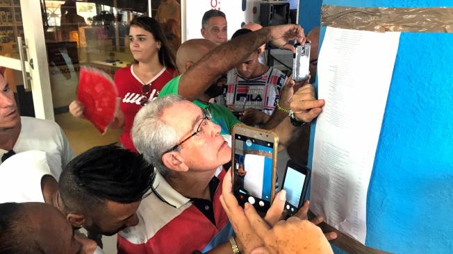 Varias personas le tomaron fotos a la lista de precios de los productos que salen a la venta en dólares en las nuevas tiendas, este lunes en La Habana, Cuba.
