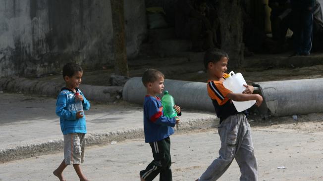 Niños palestinos llenan botellas con agua de los tanques de la Agencia de la ONU para los Refugiados Palestinos (UNRWA) en Gaza.