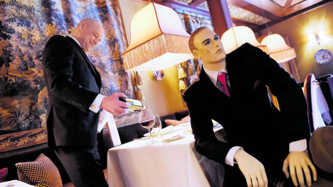 Un mesero sirve vino en una mesa con un maniquí elegantemente vestido en el restaurante The Inn at Little Washington, que tiene tres estrellas Michelin.