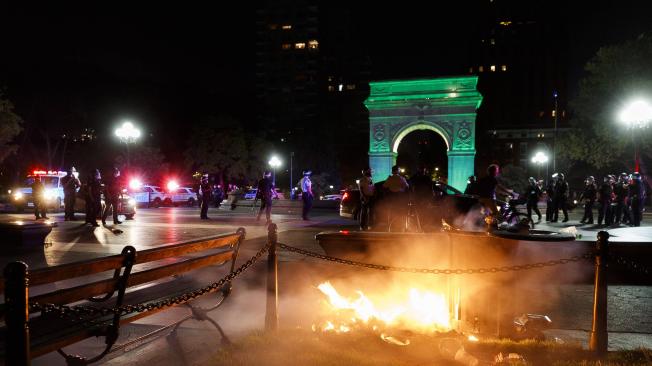 Los oficiales de policía de la ciudad de Nueva York son vistos en el fondo del incendio provocado por los manifestantes en el parque Washington Square durante las protestas por el arresto de George Floyd en Mineápolis.