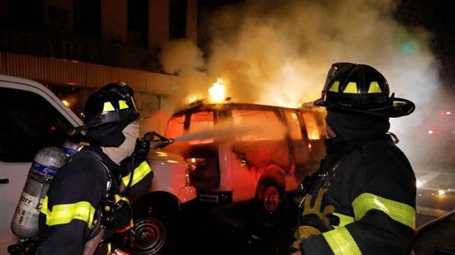 Los bomberos de la ciudad de Nueva York rocían agua sobre una camioneta de la policía incendiada por los manifestantes.