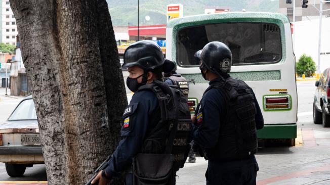 Miembros de la Policía Nacional Bolivariana se protegen detrás de un árbol durante enfrentamientos armados con integrantes de una banda criminal en el barrio La Cota 905 de Caracas.