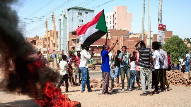 Manifestantes sudaneses levantan banderas nacionales y queman neumáticos en una calle de la capital, Jartum, el 26 de octubre de 2021.