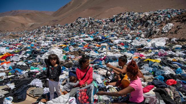 Mujeres buscan ropa usada en medio de toneladas desechadas en el desierto de Atacama, en Alto Hospicio, Iquique, Chile, el 26 de septiembre de 2021.