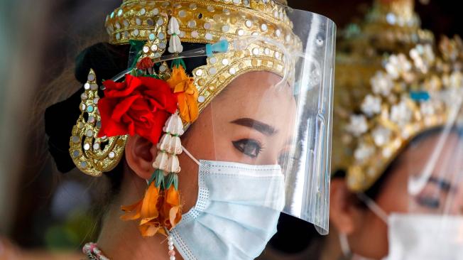 Bailarines tailandeses llevan mascarilla y protector facial durante una actuación para adorar al Señor Brahma, el dios hindú de la creación, en un punto turístico.