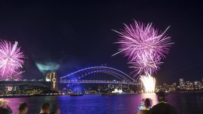 Los visitantes ven un espectáculo de fuegos artificiales cerca del Puente del puerto de Sídney durante las celebraciones de la víspera de Año Nuevo en Sídney, Australia, el viernes 31 de diciembre de 2021.