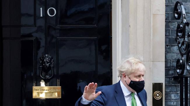 El primer ministro británico, Boris Johnson, que se cubre la cara para ayudar a mitigar la propagación del coronavirus, saluda cuando sale de 10 Downing Street en el centro de Londres el 19 de enero de 2022 para participar en la sesión semanal de Preguntas al Primer Ministro (PMQ) en la casa de los Comunes.