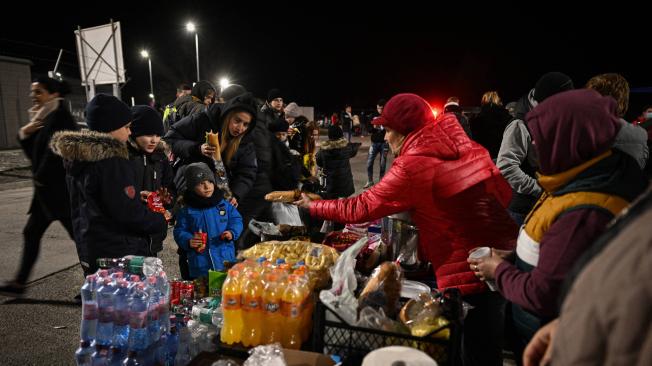 Los ucranianos (izquierda) reciben alimentos y bebidas gratis cuando ingresan a Rumania después de cruzar el río Danubio en el cruce fronterizo de Isaccea-Orlivka entre Rumania y Ucrania.