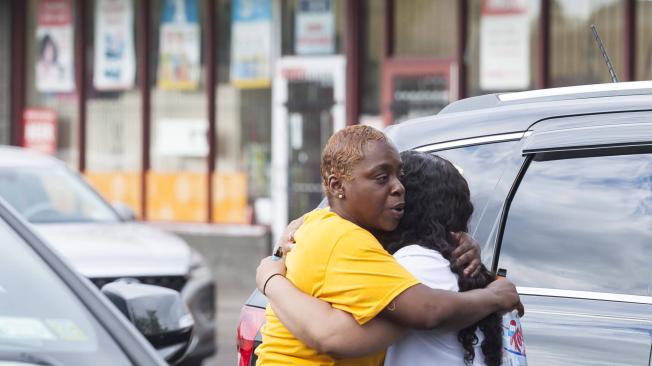 Dos personas se abrazan cerca de la escena de un tiroteo masivo en la tienda e comestibles Tops Friendly Market en Buffalo, Nueva York.