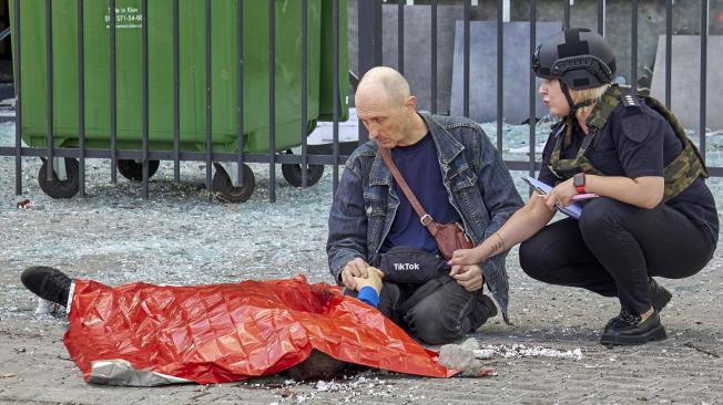 Una mujer policía calma a un hombre junto al cuerpo de un niño tras el lanzamiento de un cohete ruso contra una parada de autobús en Járkov, Ucrania, el 20 de julio de 2022.