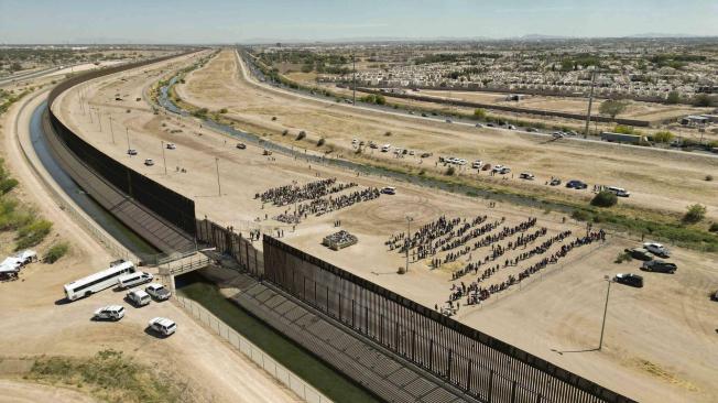 Cientos de migrantes mientras esperan junto al muro fronterizo en El Paso, Texas (EE.UU).