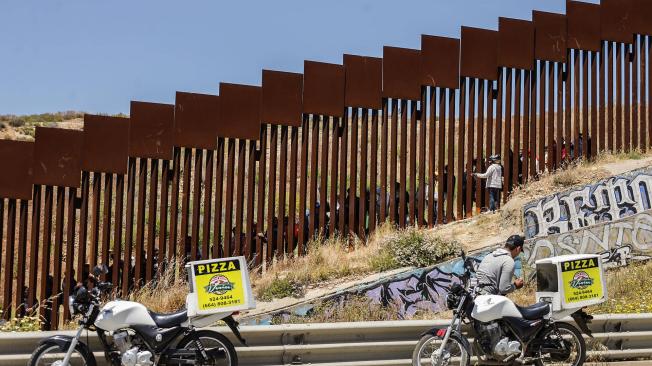 Repartidores de comida rápida entregan pedidos a migrantes en el muro fronterizo hoy, en la ciudad de Tijuana, Baja California.