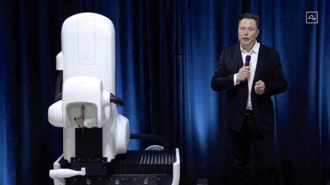 El controvertido magnate Elon Musk, junto al robot quirúrgico que sería el encargado de insertar el implante a los humanos.