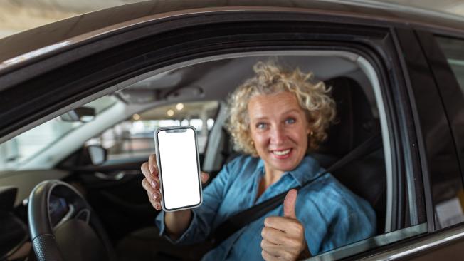 Front view of a mid adult woman using a smart phone for car rental. Car Insurance. Smart technology.