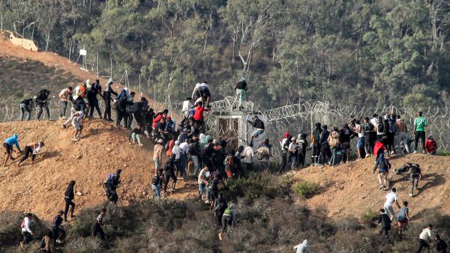 Migrantes asaltan una valla de alambre de espino mientras intentan cruzar la frontera terrestre con el enclave africano español de Ceuta, cerca de Fnideq, en el norte de Marruecos.