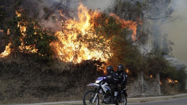 AME2193. QUITO (ECUADOR), 24/09/2024.- Agentes de la Policía de Ecuador pasan frente a un incendio forestal este martes, en el sector de Guapulo en Quito (Ecuador). EFE/ Santiago Fernández