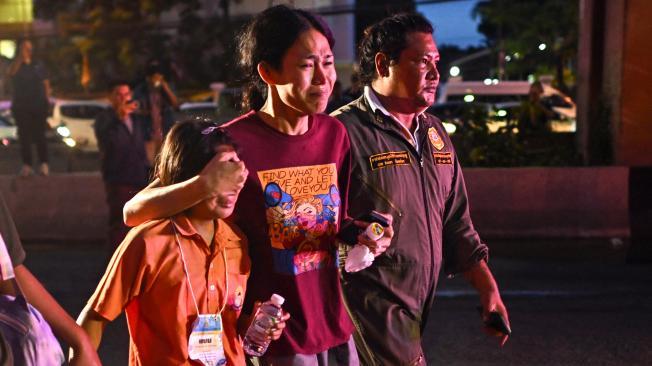 A relative (C) of a student who died in a bus fire covers the eyes of a young relative who was travelling on a separate bus on the same school trip as they walk past the burnt bus wreckage on the outskirts of Bangkok on October 1, 2024. A devastating fire tore through a Thai bus carrying 44 students and teachers on a school trip on October 1, officials said, with up to 25 feared dead. (Photo by Manan VATSYAYANA / AFP)