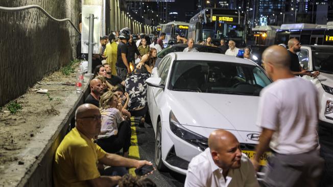 Varias personas se cubren detrás de vehículos en una autopista en Tel Aviv durante el ataque de Irán.