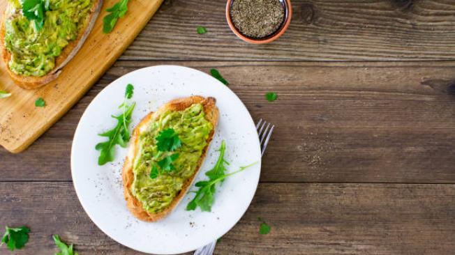 Avocado toast on a white plate on a rustic wooden table. 
Avocado toast, desayuno típicoSpace for copy on the right of the image. 
Stock photo