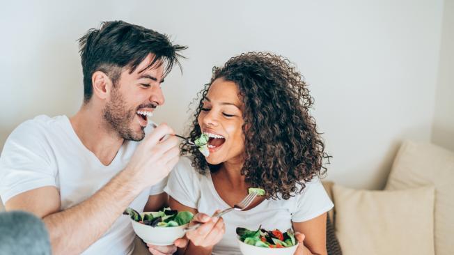 Happy man feeding his girlfriend with salad