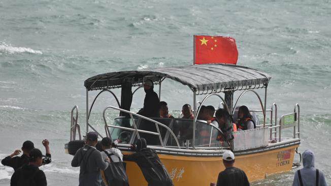 Los trabajadores empujan un barco, visto con una bandera china, hacia las olas en una playa de la isla Pingtan, el punto más cercano en China a la isla principal de Taiwán, en la provincia china de Fujian, en el sudeste, el 15 de octubre de 2024.