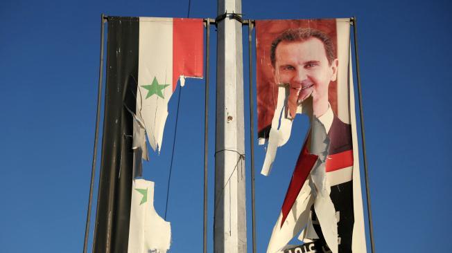 Una valla publicitaria con la imagen del presidente sirio Bashar al-Assad y una bandera nacional son arrancadas por combatientes antigubernamentales en Alepo.