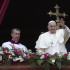Se ve al Papa Francisco, acompañado de otros sacerdotes, desde el balcón. Él est´pa levantando la mano, saludando a los presentes. Detrás de él está un crucifijo.