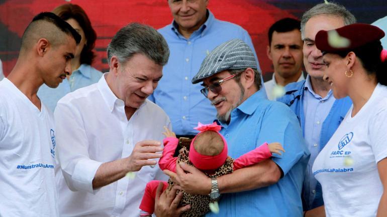 El presidente Juan Manuel Santos (i) y el jefe máximo de las Farc, Rodrigo Londoño 'Timochenko', sostienen y saludan al bebé de un guerrillero durante la ceremonia de dejación de armas.