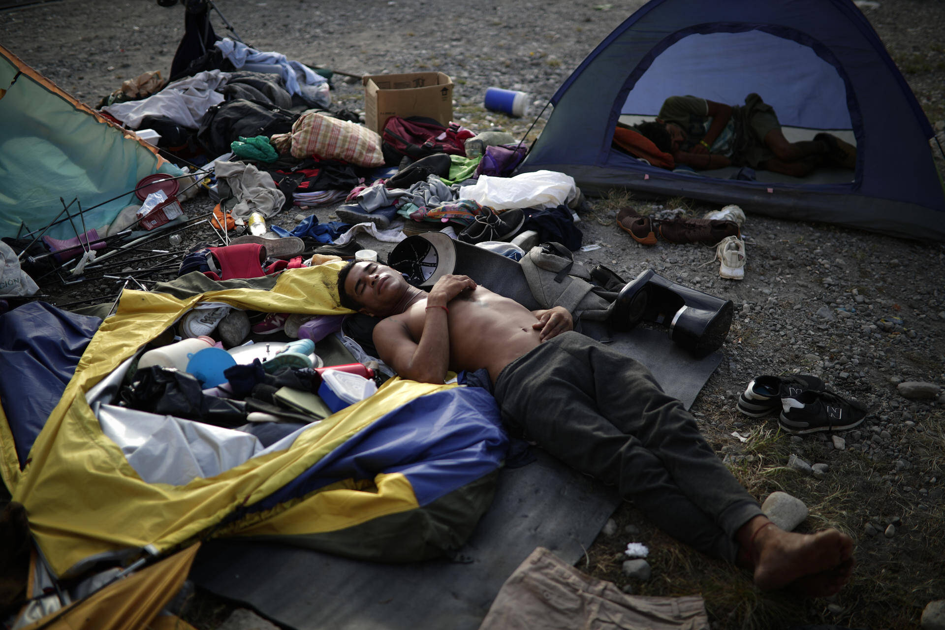Un migrante duerme mientras decenas esperan su traslado.