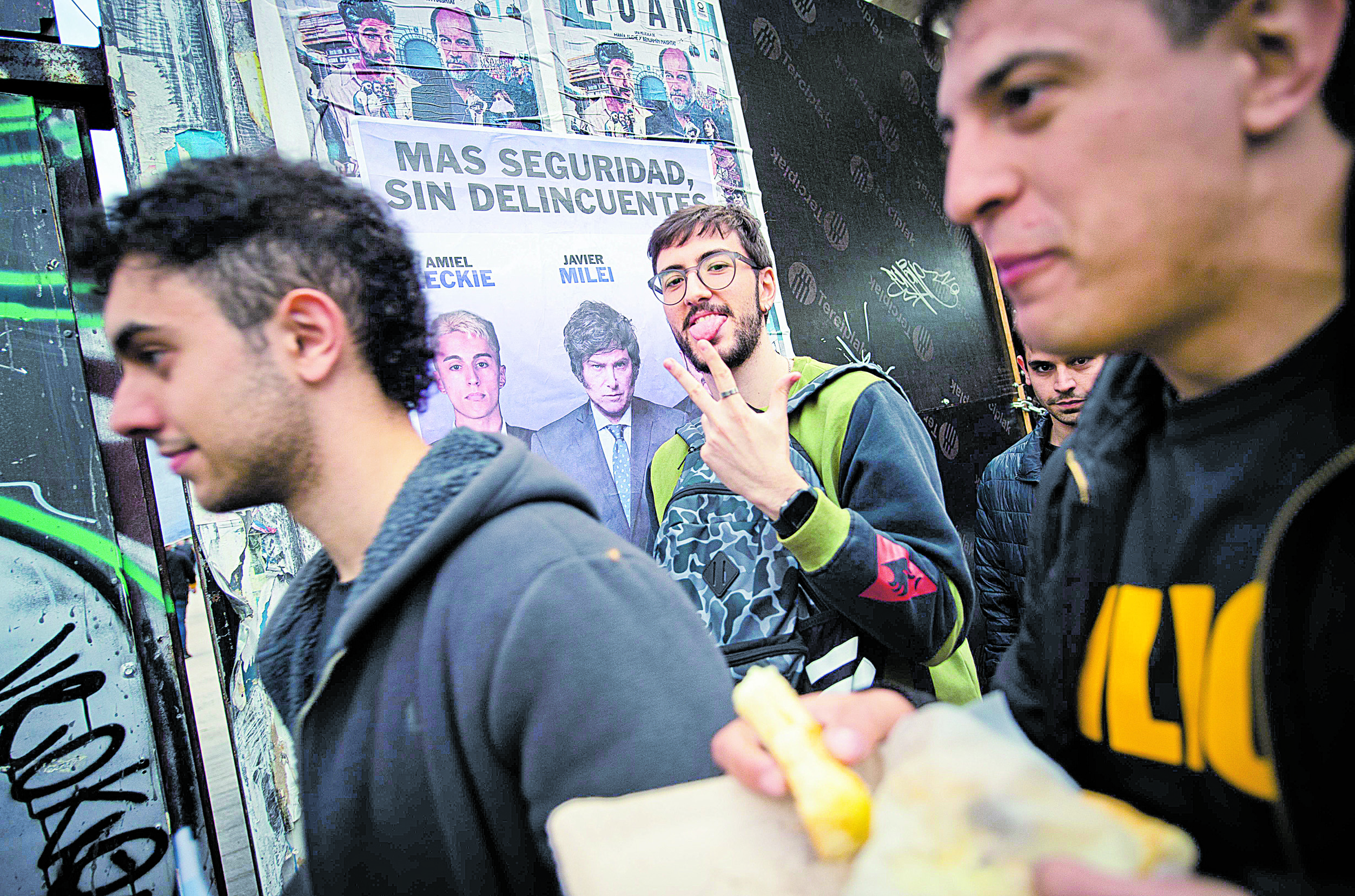 Jóvenes simpatizantes de Javier Milei pasan junto a un cartel a favor de él durante la campaña presidencial argentina, en Buenos Aires.